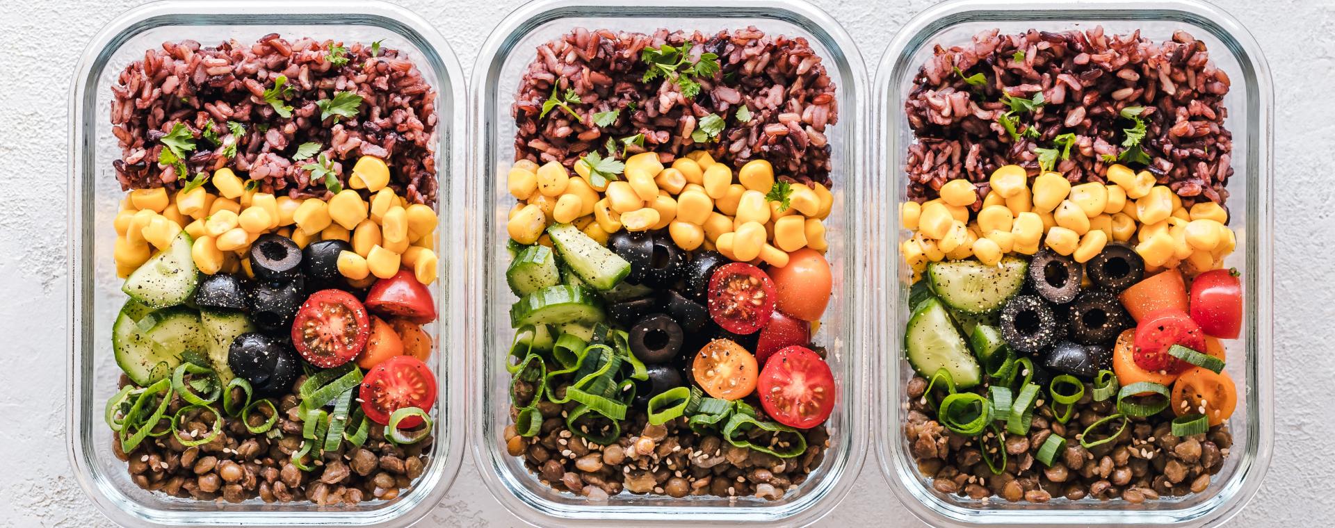 three glass tupperware boxes fillied with beans, pulses, fruit; they're all look brightly coloured, green, yellow, reds, brown.