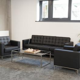 black sofa, two black arm chairs and glass coffee table with a chess set, plant in the corner and on the window sill